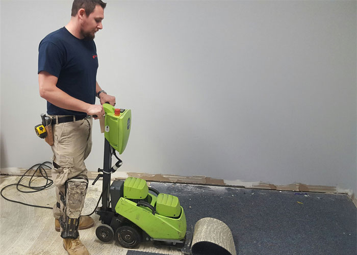 Flooring installer removing carpeted floors with large tool power stripper