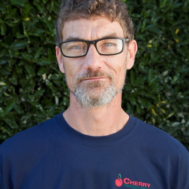 Mark Rogers headshot in front of green bush