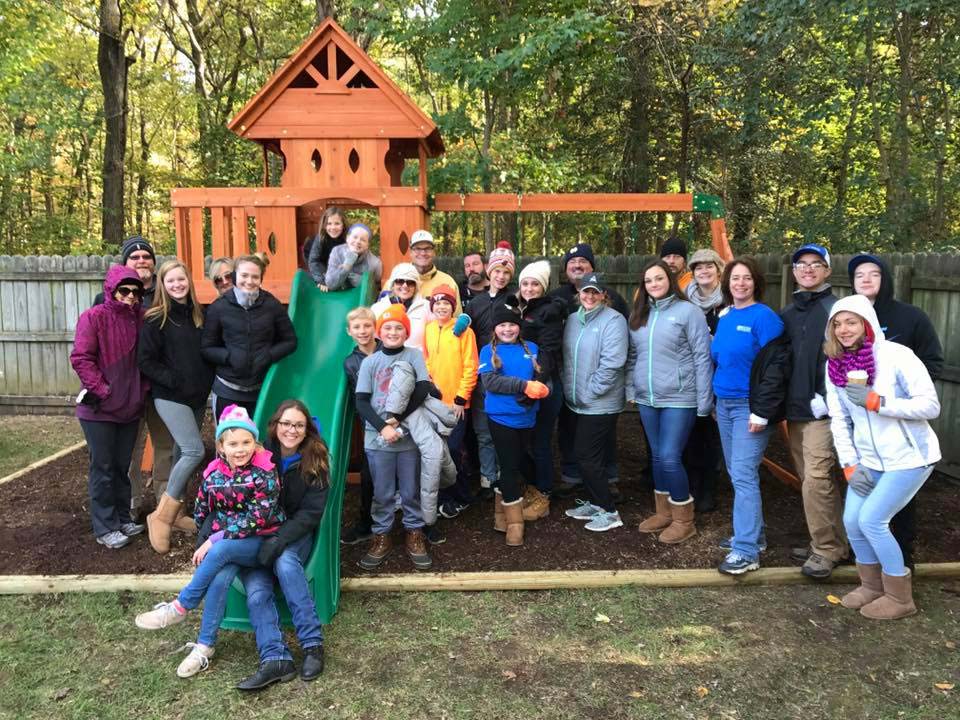 Large group standing at playground in front of woods wearing sweatshirts and jackets