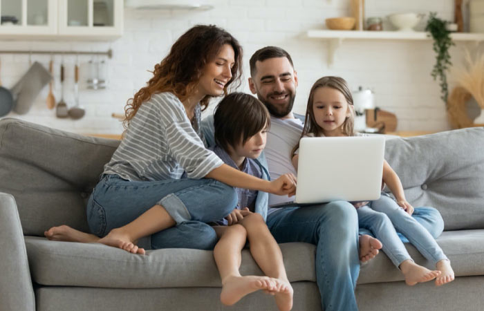Family of four sitting on the couch and excitedly shopping online with a white laptop