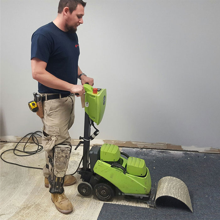 Flooring installer removing carpeted floors with large tool power stripper
