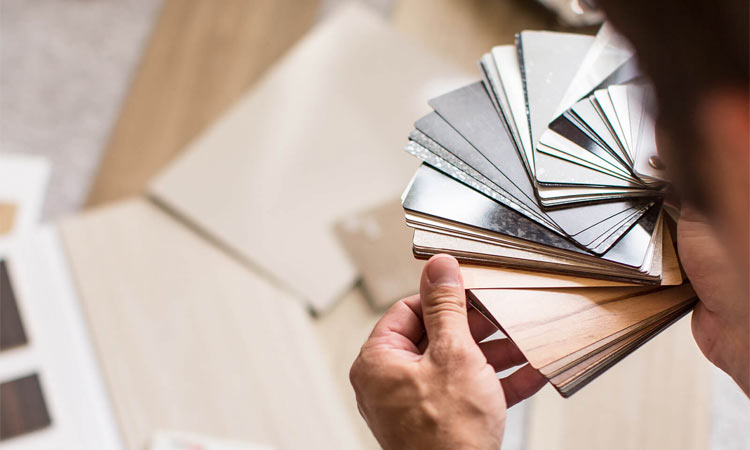 Person holding product swatches of various colors with flooring samples in the background